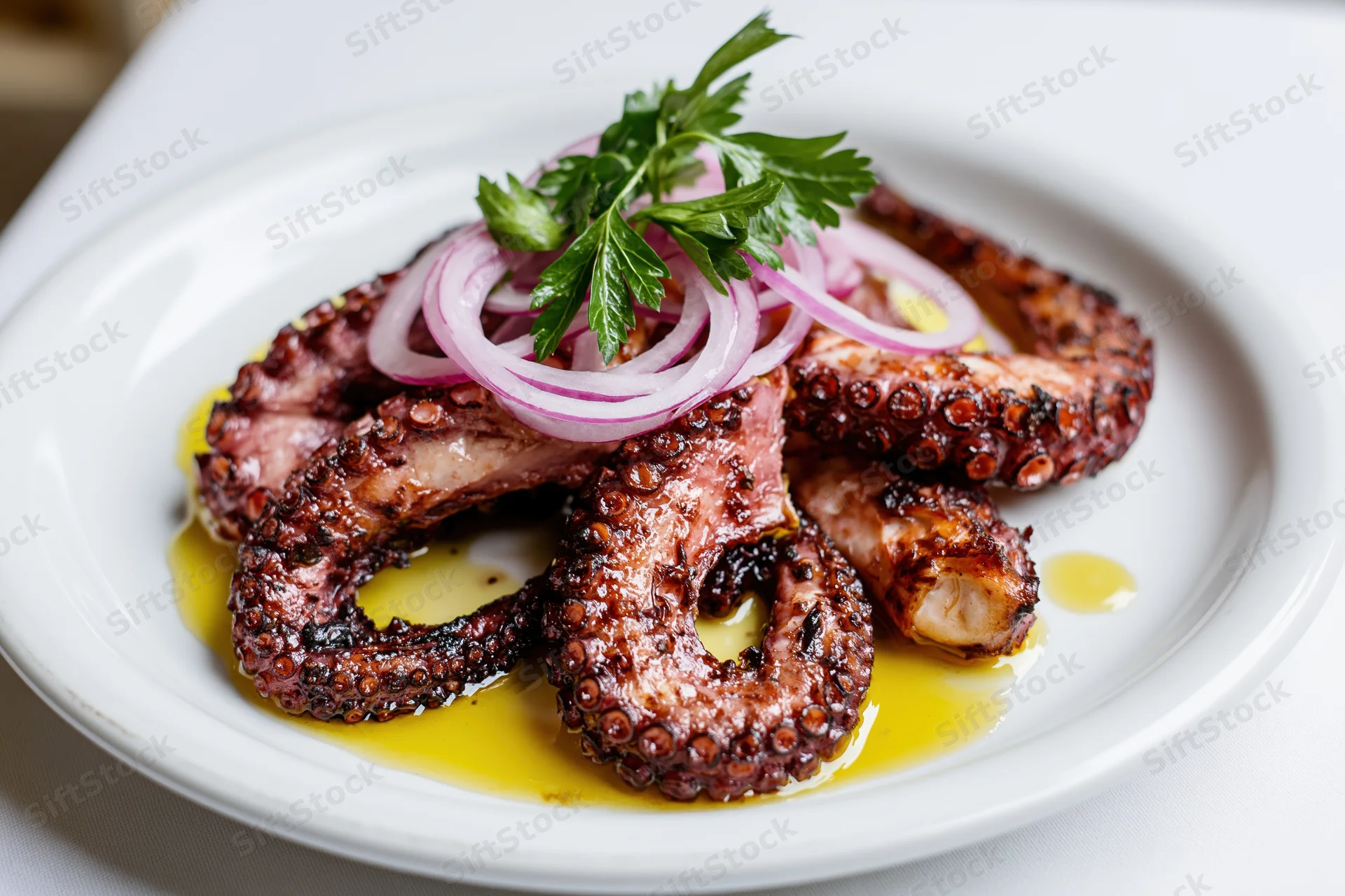 Grilled octopus tentacles arranged on a white ceramic plate with olive oil, red onion, and parsley garnish