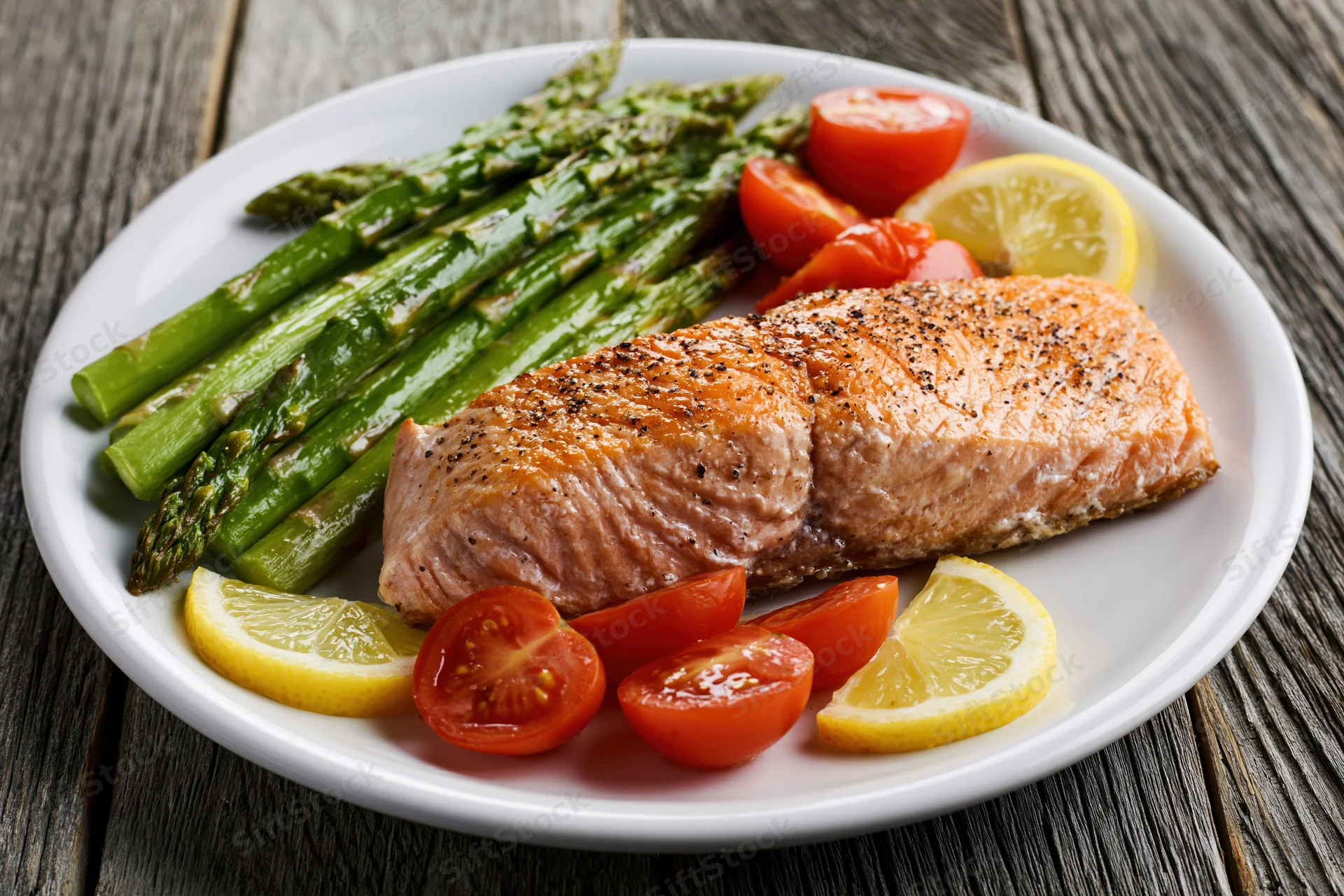 Grilled salmon fillet with steamed asparagus and lemon slices on a white plate on wooden table