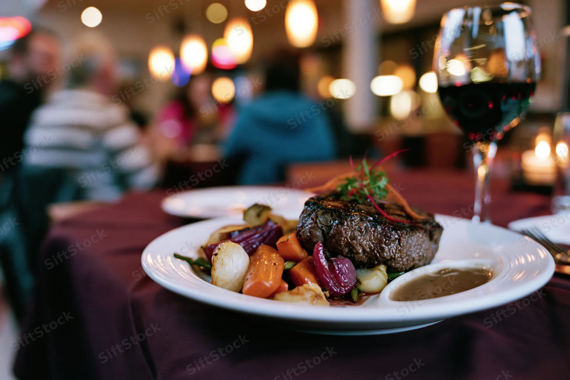 Grilled steak with roasted vegetables and garnish on a white plate at a restaurant table with wine glass and candlelit ambiance