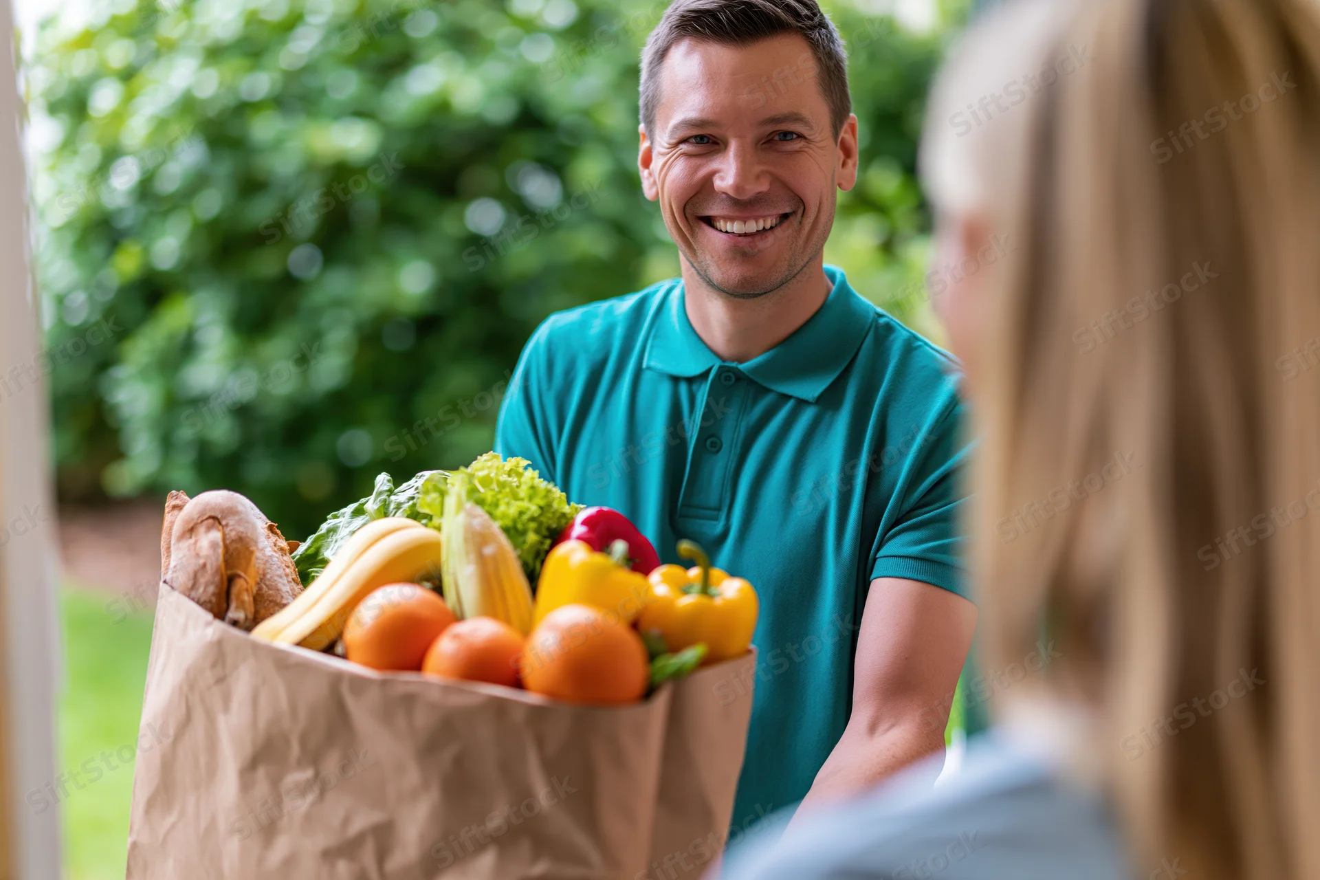 Smiling delivery man handing a grocery bag filled with fresh produce to a woman at her door
