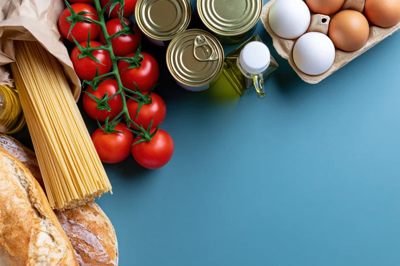 Grocery staples arranged along the right edge of a flat lay on a blue surface