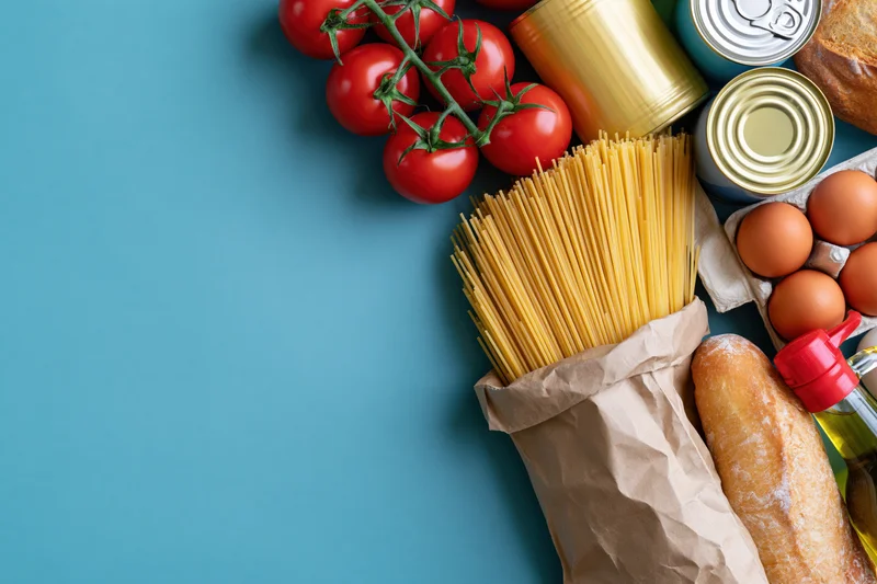 Grocery staples arranged along the right edge of a flat lay on blue background with copyspace