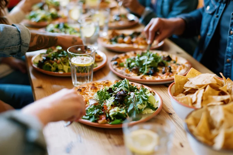 Friends sharing pizza and salad at a wooden dining table