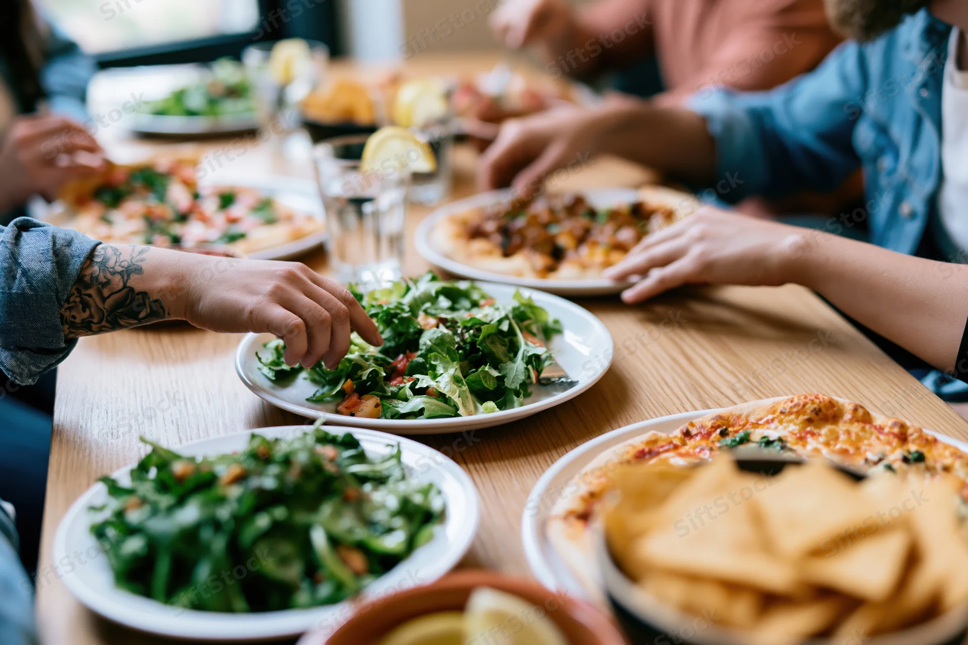 Friends sharing pizza and salad at a wooden dining table during a casual meal
