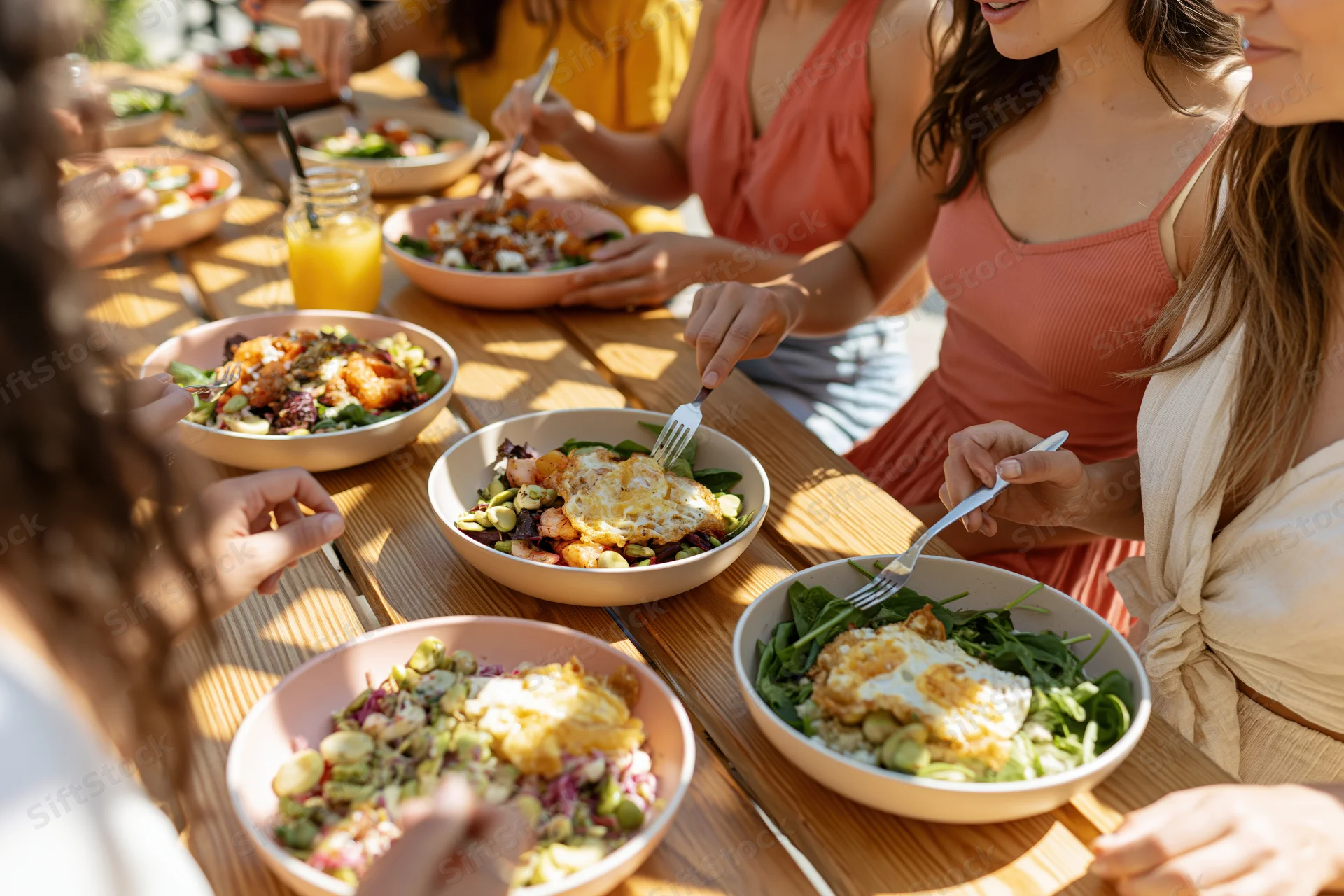 Young women sharing healthy brunch bowls at a wooden table outdoors
