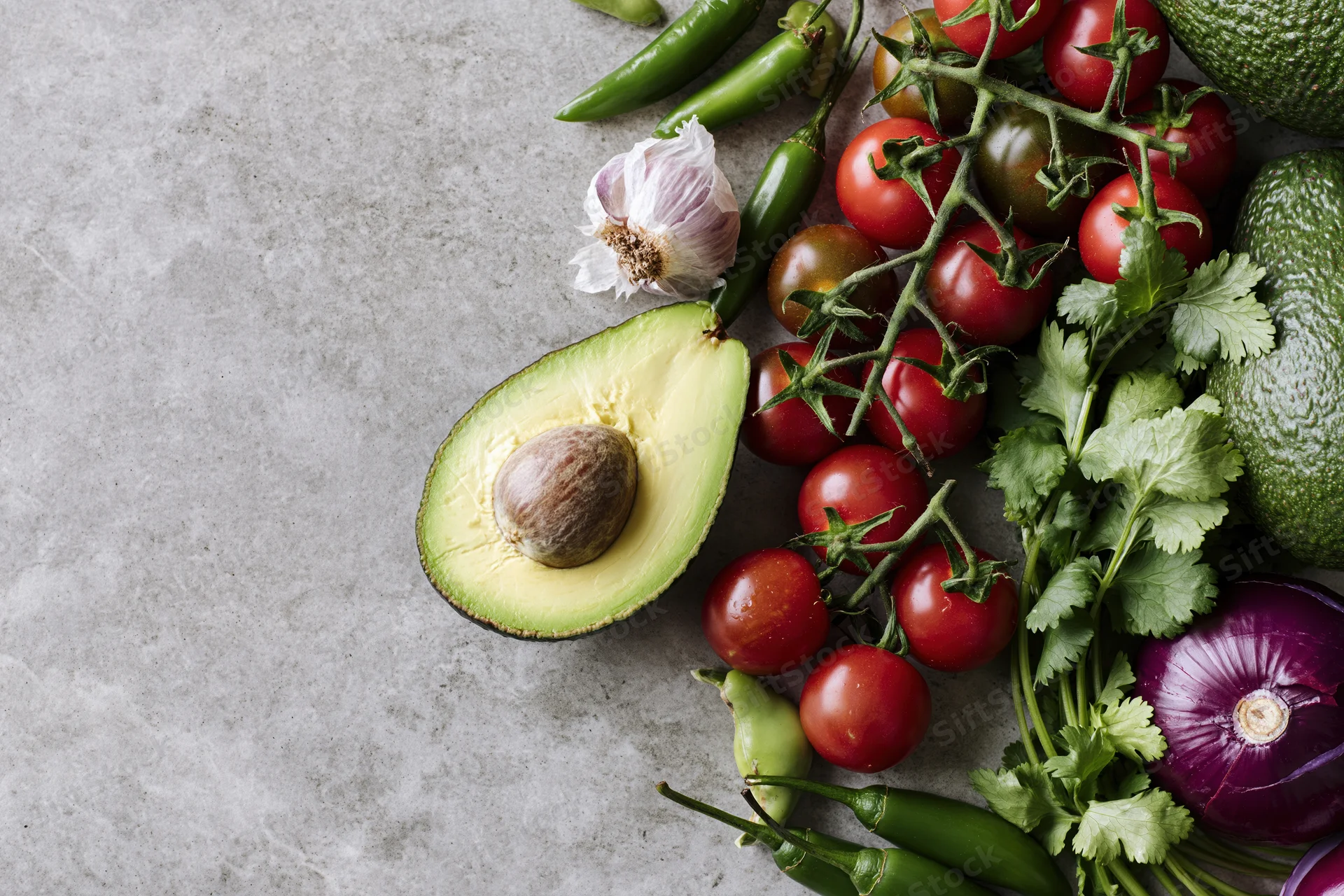 Guacamole ingredients arranged on a concrete surface with copyspace on the left