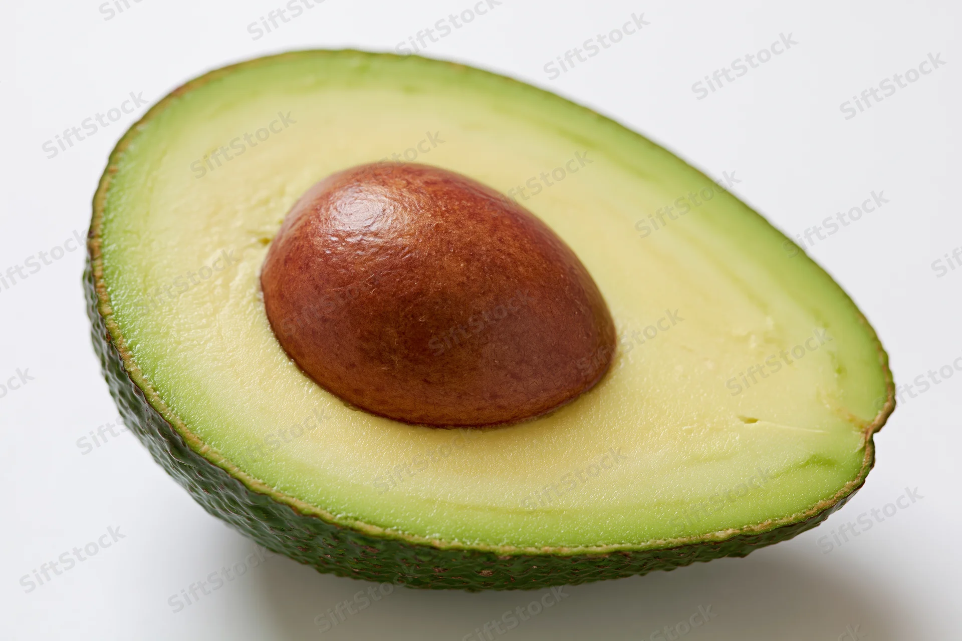 Half avocado cut lengthwise showing brown pit nestled in creamy green flesh on white background
