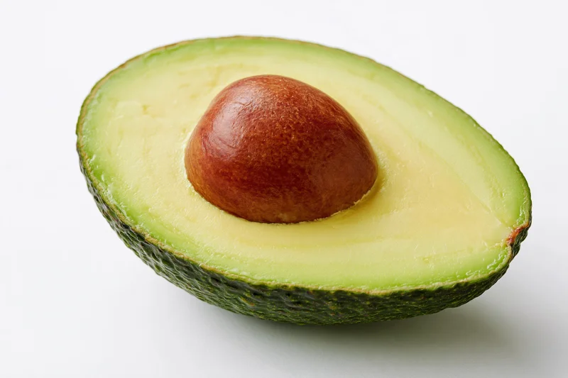 Half avocado cut lengthwise showing brown pit on white background