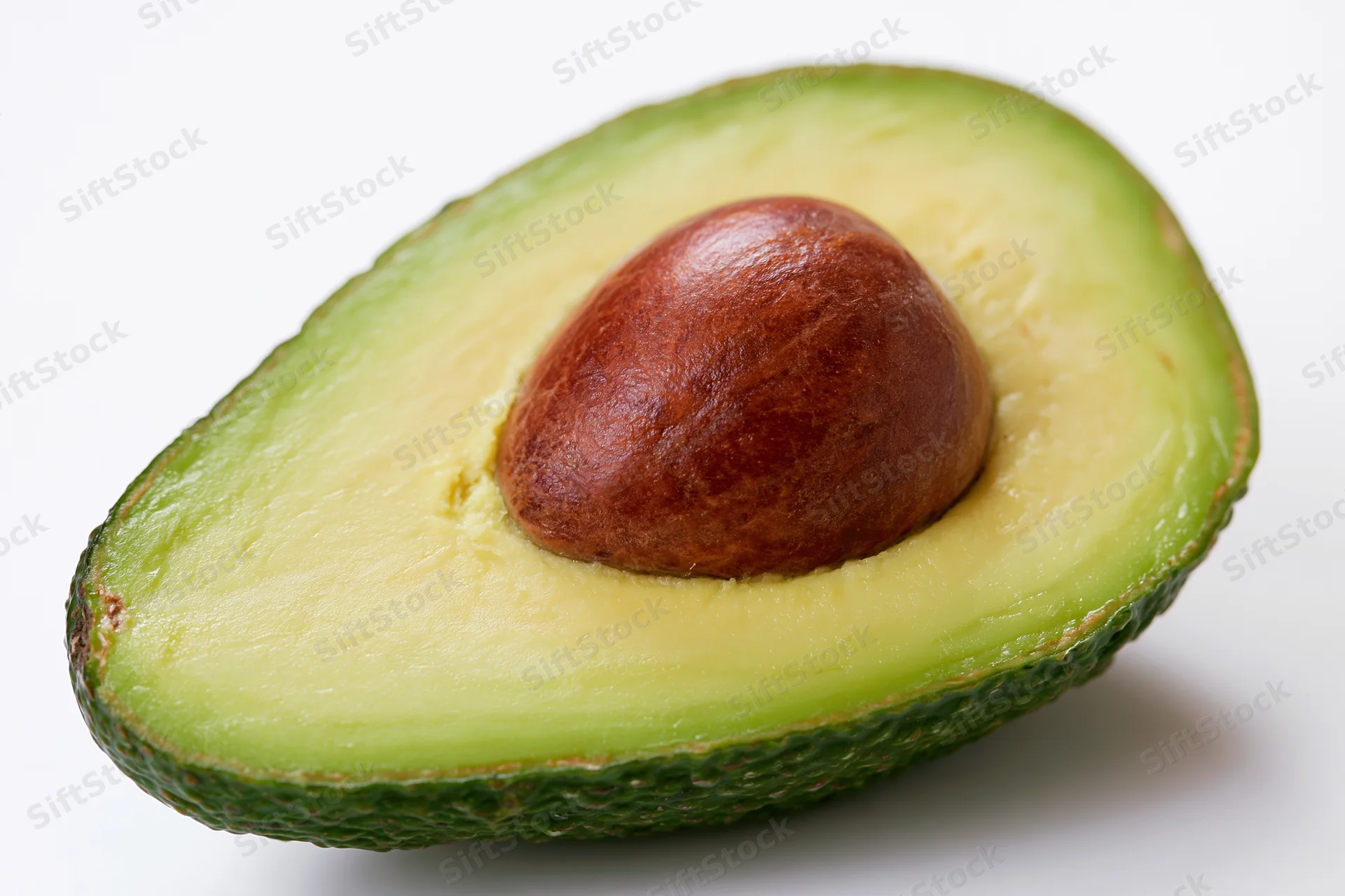 Half avocado cut lengthwise showing brown pit nestled in green flesh on white background