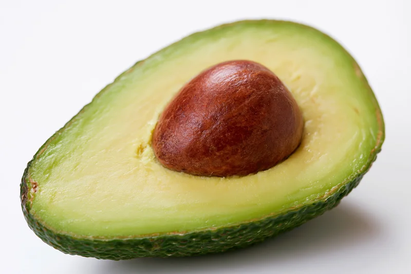 Half avocado cut lengthwise showing brown pit nestled in green flesh on white background