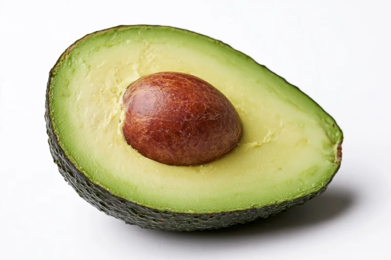 Half avocado cut lengthwise showing brown pit on white background