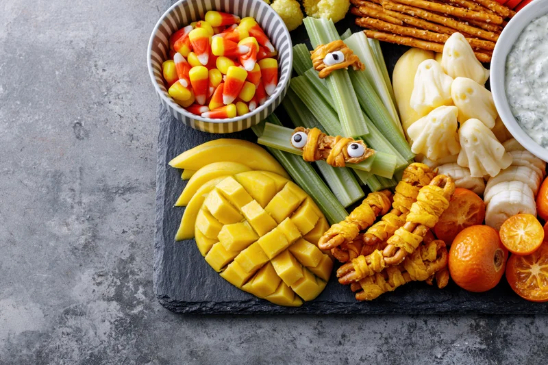 Halloween-themed snack board with decorated celery, fruit, cheese and candy arranged on slate tray