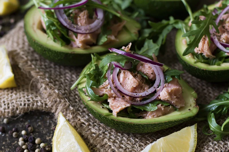 Halved avocados filled with flaked salmon and red onion rings