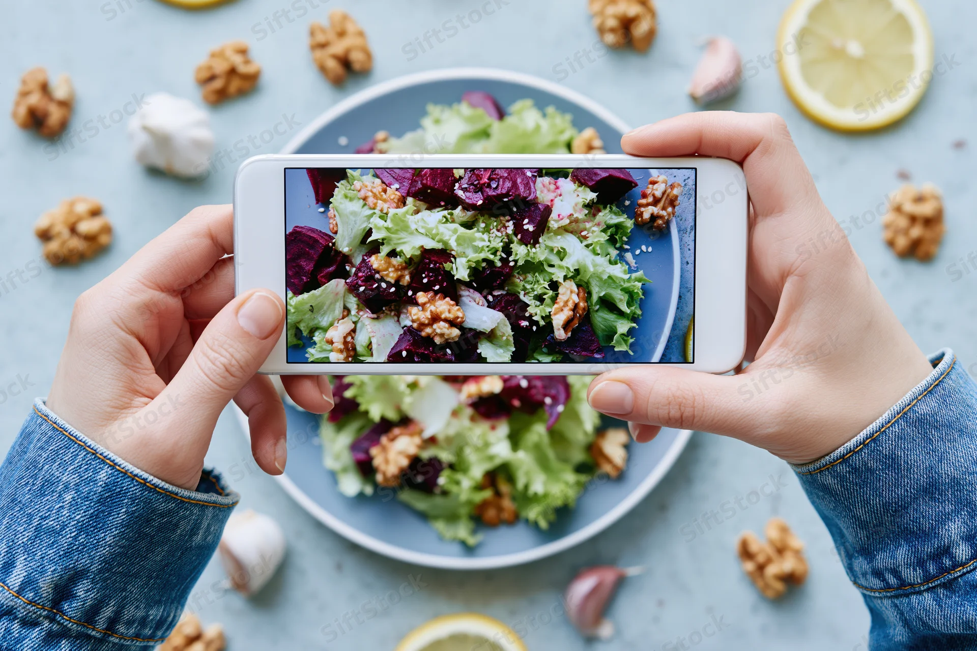 Hands holding smartphone photographing salad on plate with walnuts and lemon slices