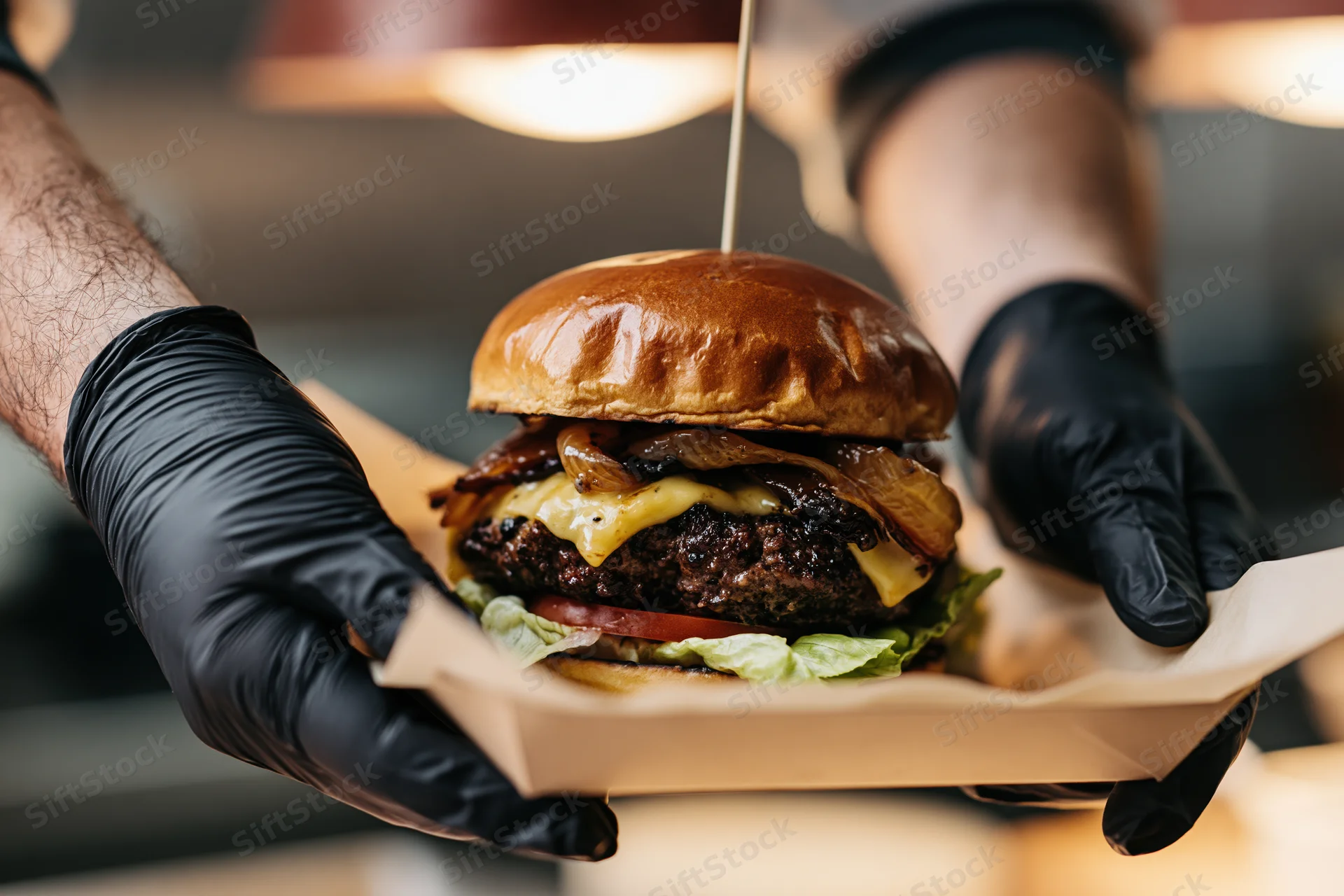 Hands in black nitrile gloves holding a cheeseburger on a paper tray
