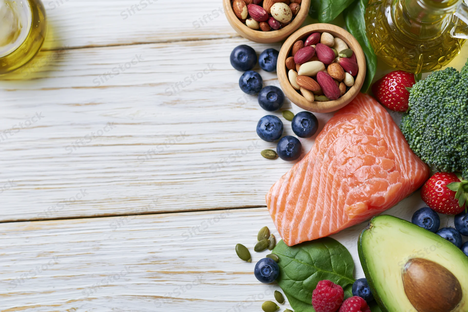 Salmon fillet with avocado, broccoli, berries, nuts and olive oil arranged on whitewashed wooden table