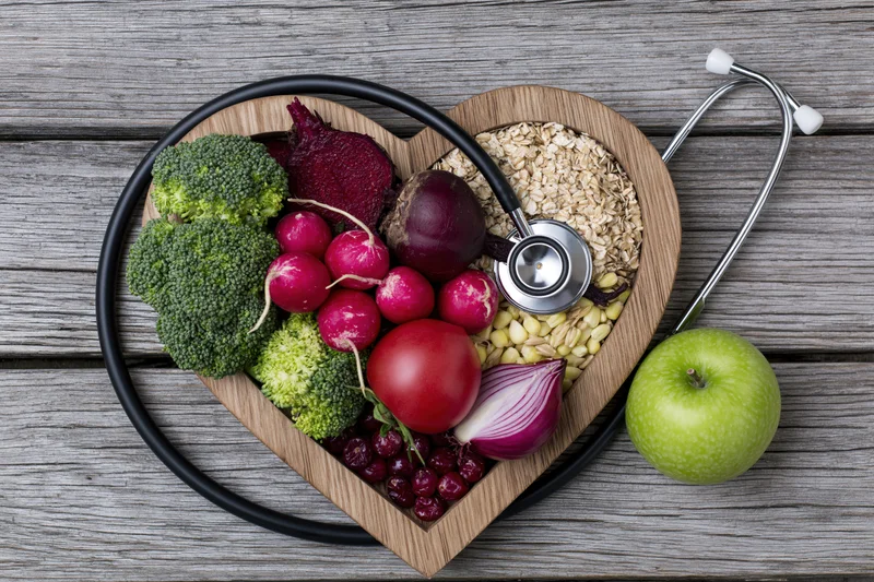 Heart-shaped wooden tray filled with vegetables and grains with stethoscope on rustic wood surface