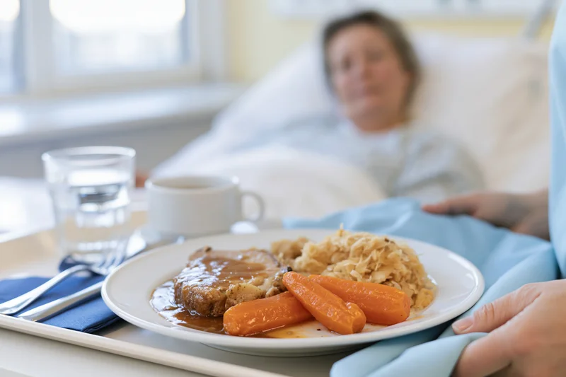 Hospital meal tray with roast beef, carrots and cabbage served to a patient in bed