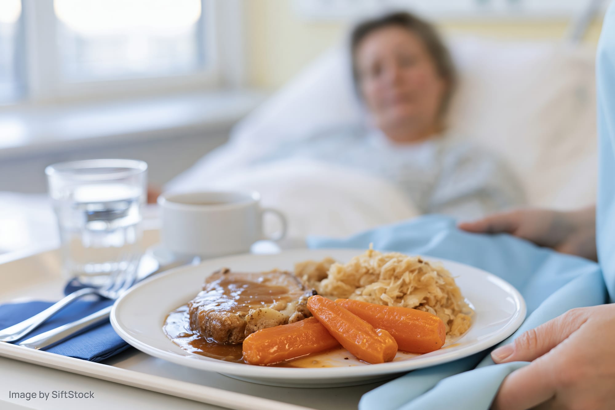 Hospital meal tray with roast beef, carrots and cabbage served to a patient in bed