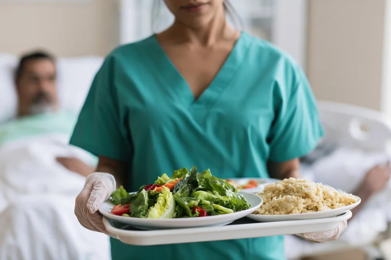 Nurse holding a tray with salad and rice in a hospital room with a patient in bed