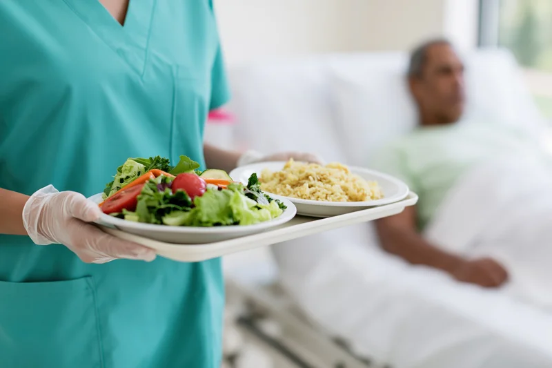 Nurse holding a tray with salad and rice for a patient in a hospital bed