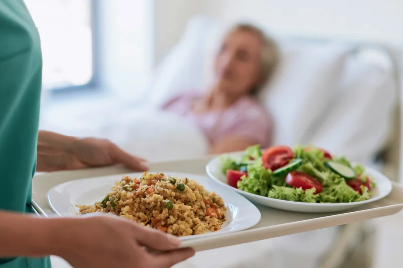 Nurse holding meal tray with salad and rice dish for patient in bed
