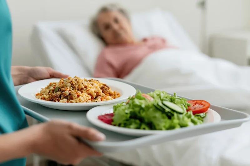 Caregiver holding meal tray with food for patient in hospital bed