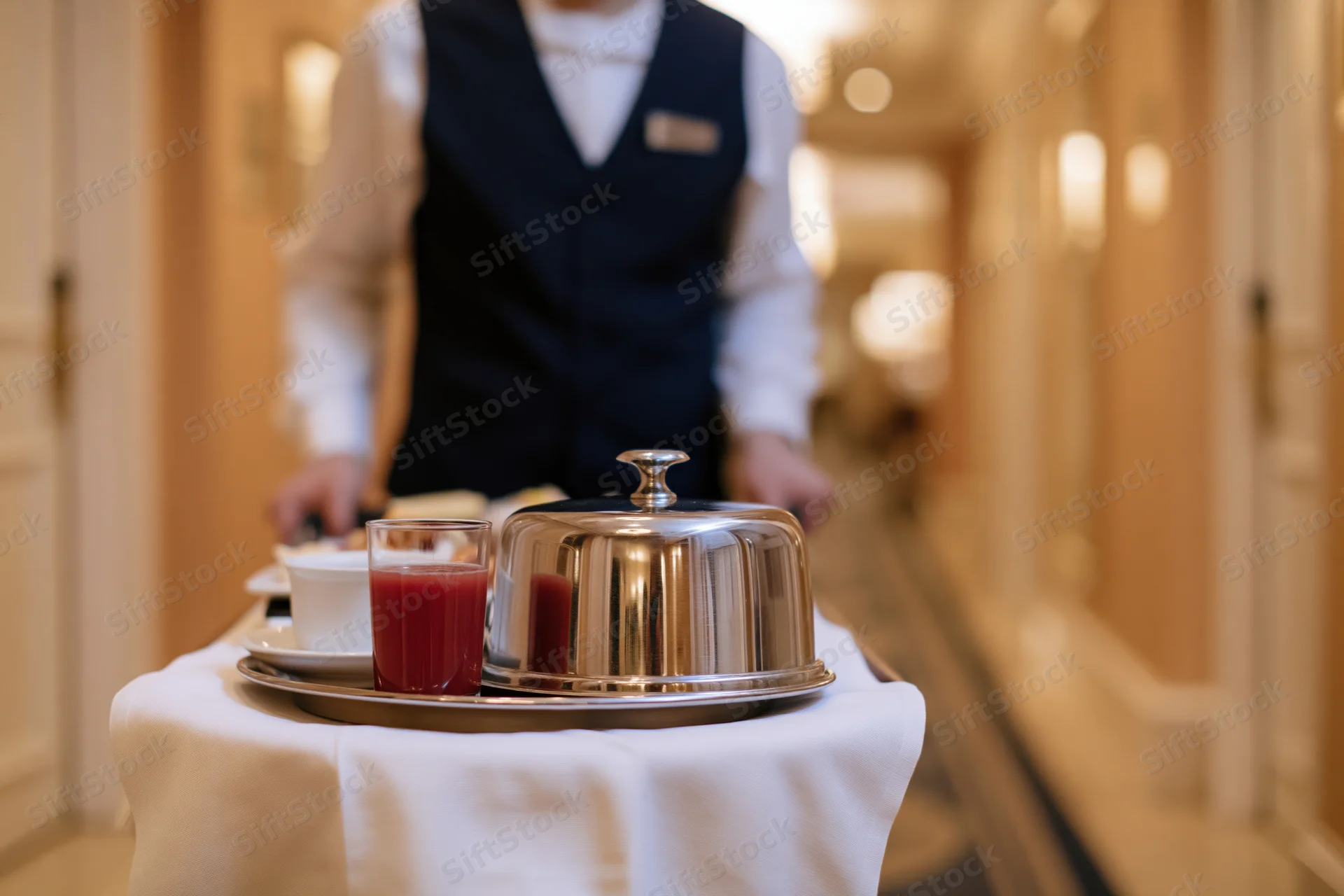 Hotel attendant pushing a room service tray with covered dish and drinks down a hallway