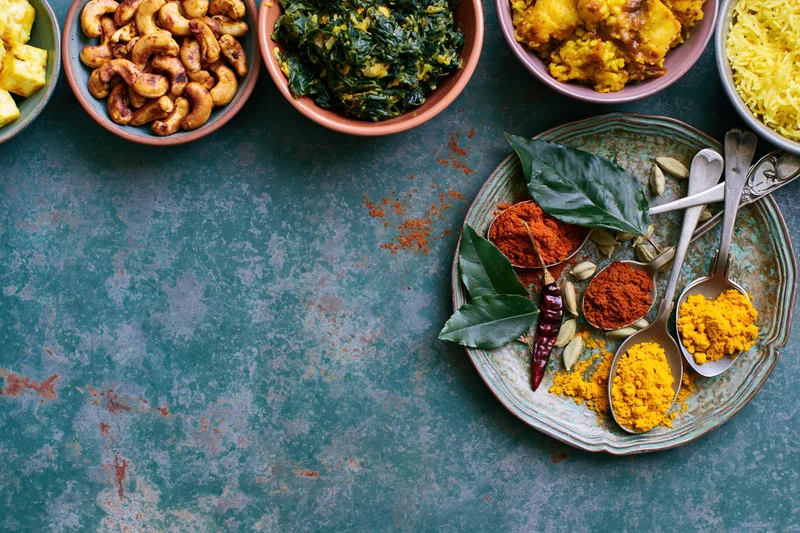 Indian food spread with spices and dishes arranged along the top edge of a dark teal surface