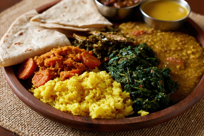 Indian thali meal served on a round wooden plate with yellow rice, lentils, spinach curry, and flatbread