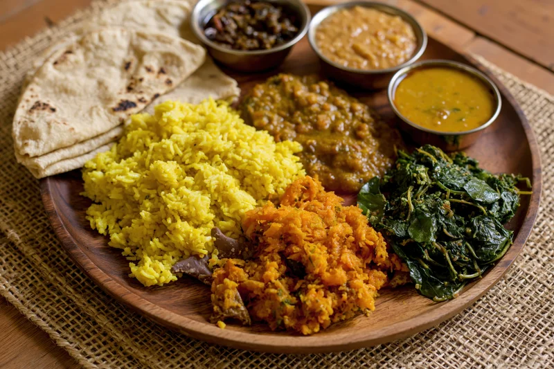 Indian thali meal served on a round wooden plate with yellow rice, curries, lentils, spinach, and flatbread on a woven mat