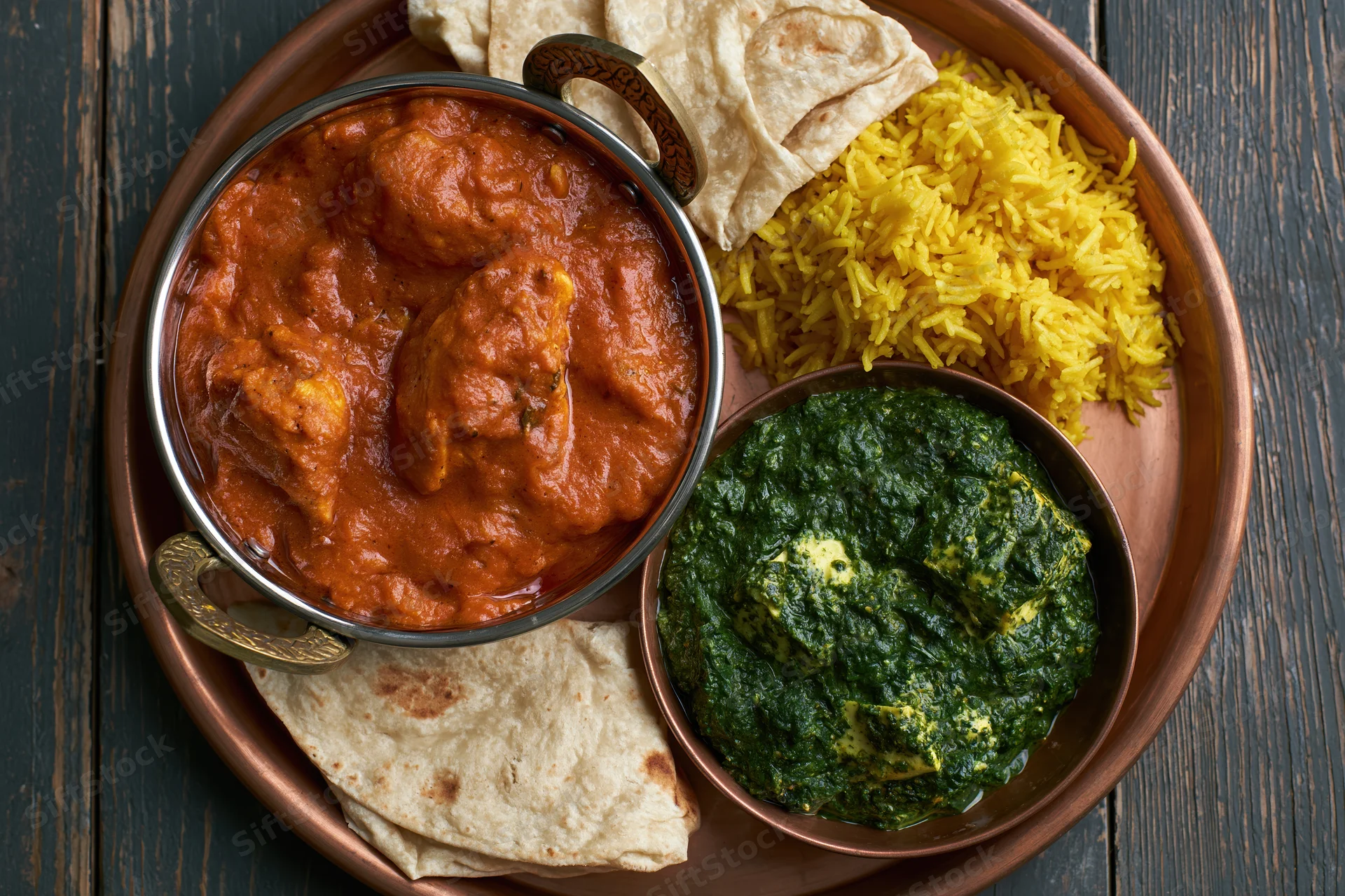 Indian thali with butter chicken curry, saag, yellow rice, and naan on a copper tray