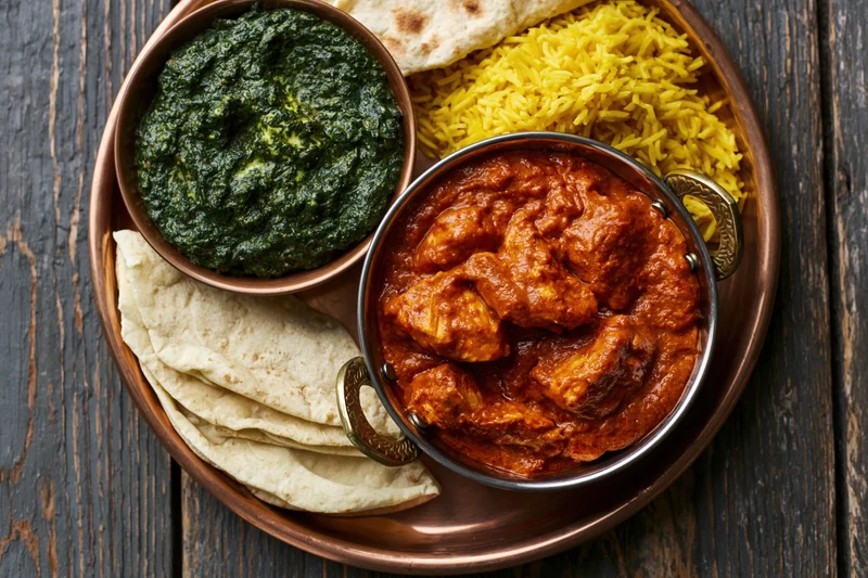 Indian thali with butter chicken, palak paneer, yellow rice, and naan on a copper tray