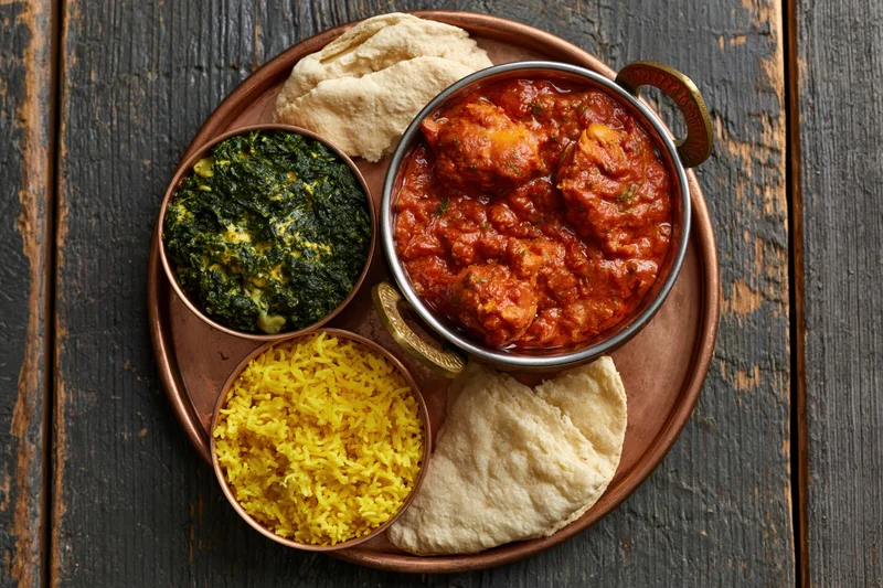 Indian thali with curry, rice, spinach, and naan on a copper tray on dark wooden table