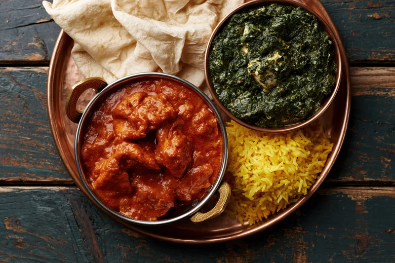 Indian thali with chicken tikka masala, palak paneer, basmati rice and naan on a copper tray on wooden table