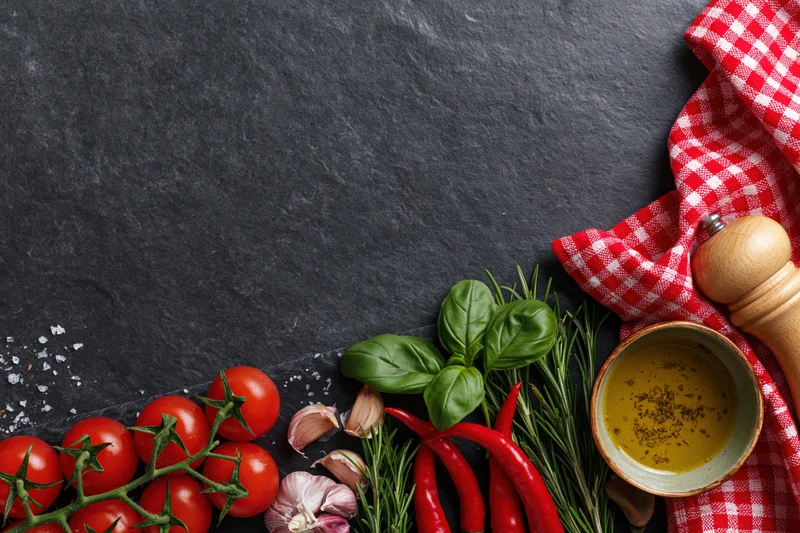 Fresh italian cooking ingredients arranged along the bottom edge of a dark slate surface with copyspace above