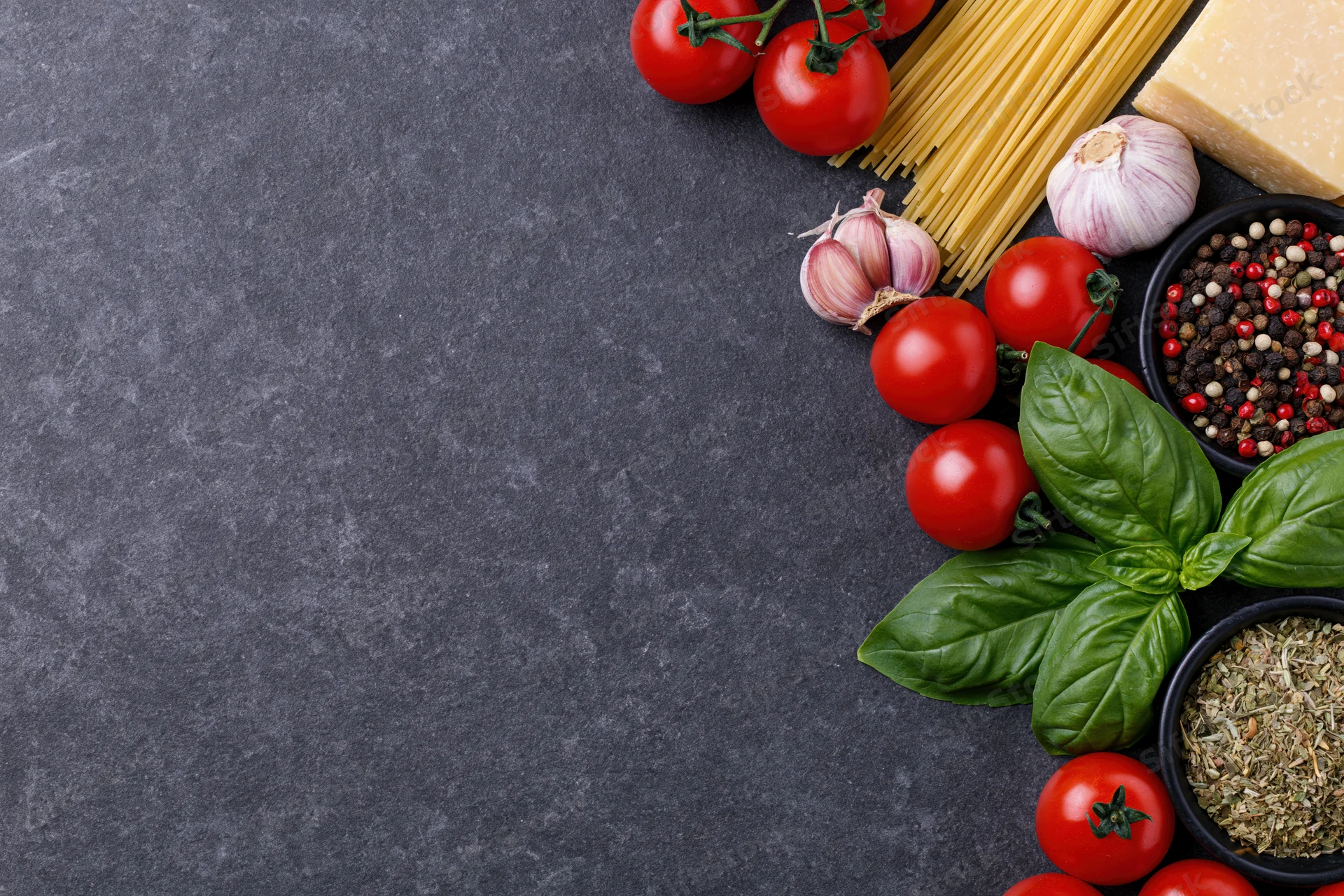 Italian cooking ingredients arranged along the right edge of a dark countertop with copyspace on the left