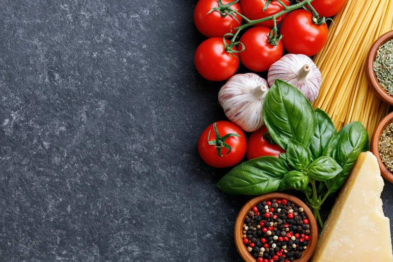 Italian cooking ingredients arranged along the right edge of a dark stone surface with copyspace on the left