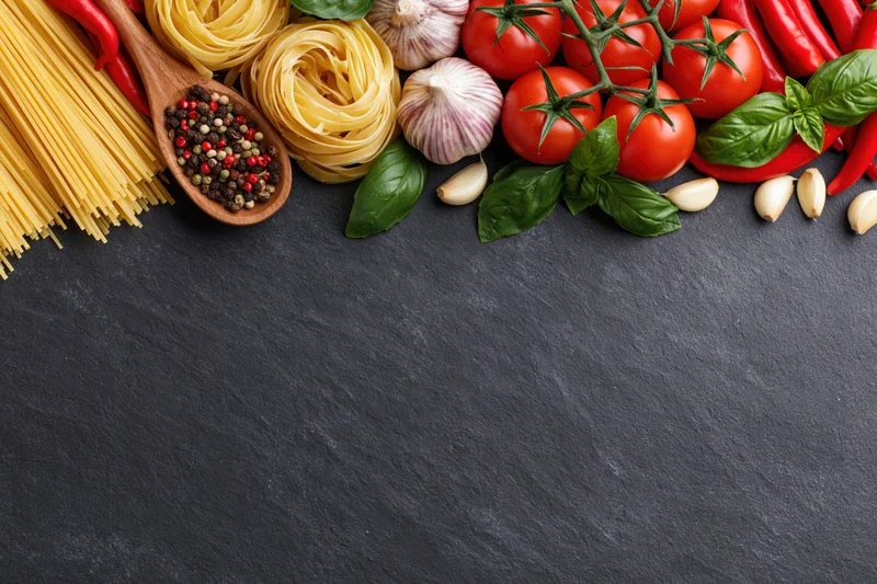 Italian cooking ingredients arranged along the top edge of a dark slate surface with copyspace below