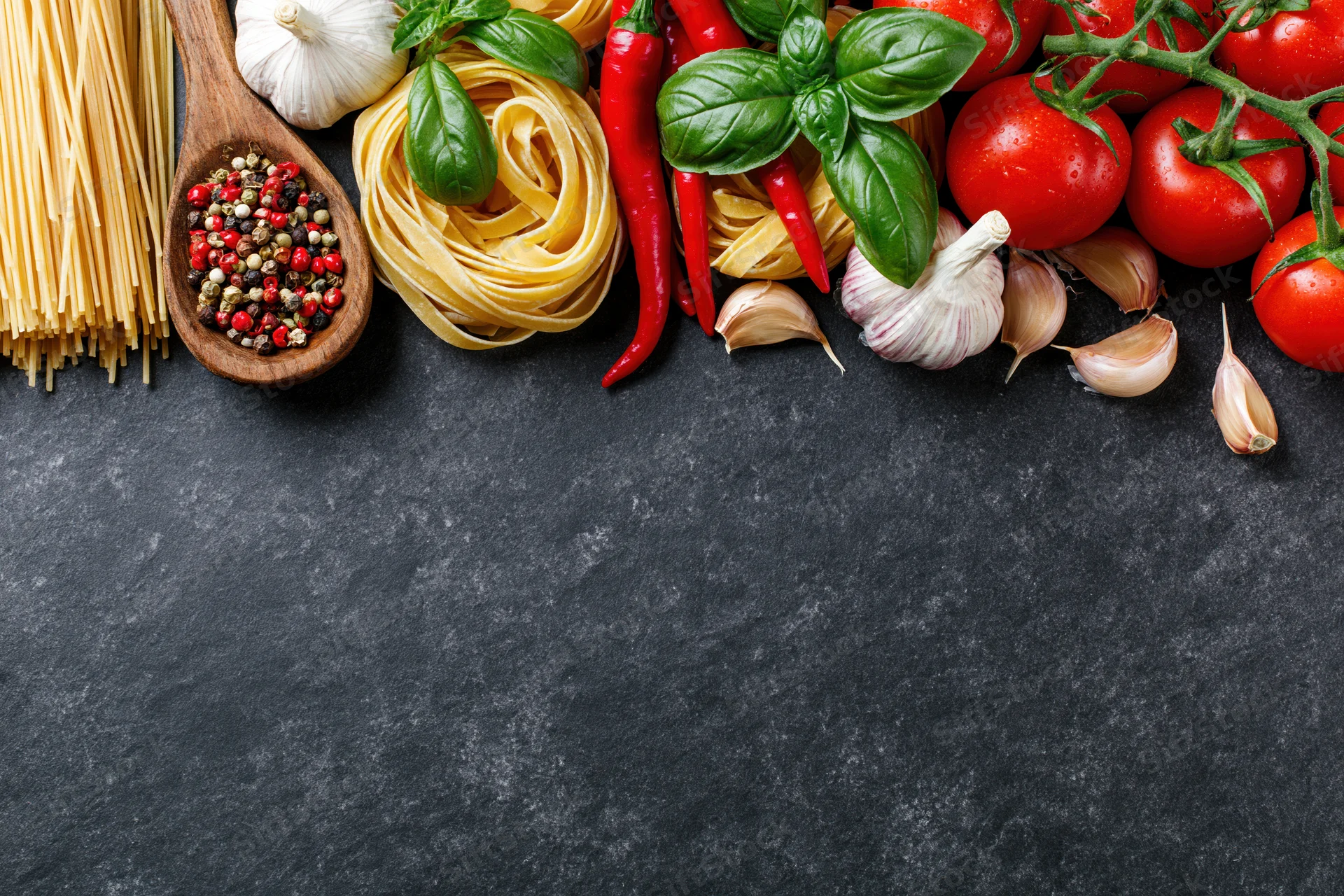 Italian cooking ingredients arranged along the top edge of a dark surface with copyspace below