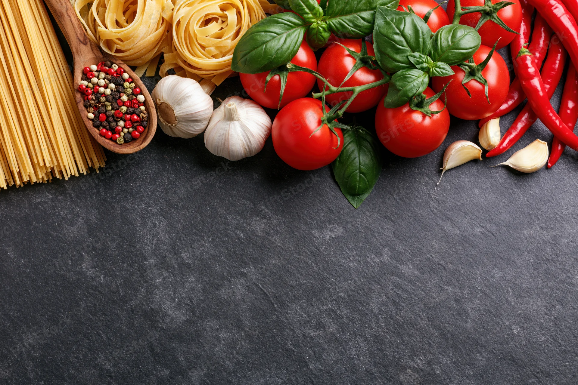 Fresh italian cooking ingredients arranged along the top edge of a dark slate surface
