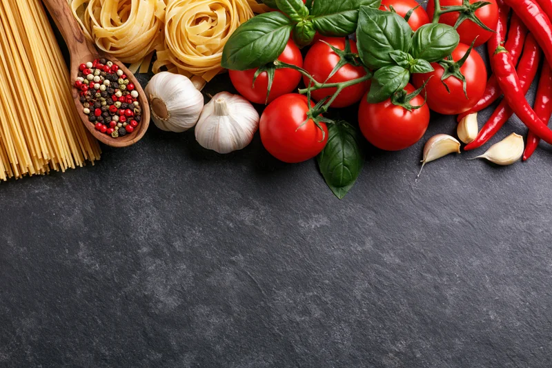 Fresh italian cooking ingredients arranged along the top edge of a dark slate surface
