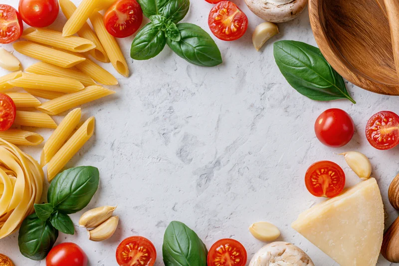 Italian cooking ingredients arranged as a flat lay border on a white marble surface