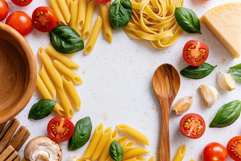 Italian cooking ingredients arranged in a flat lay border on a white countertop with copyspace in center