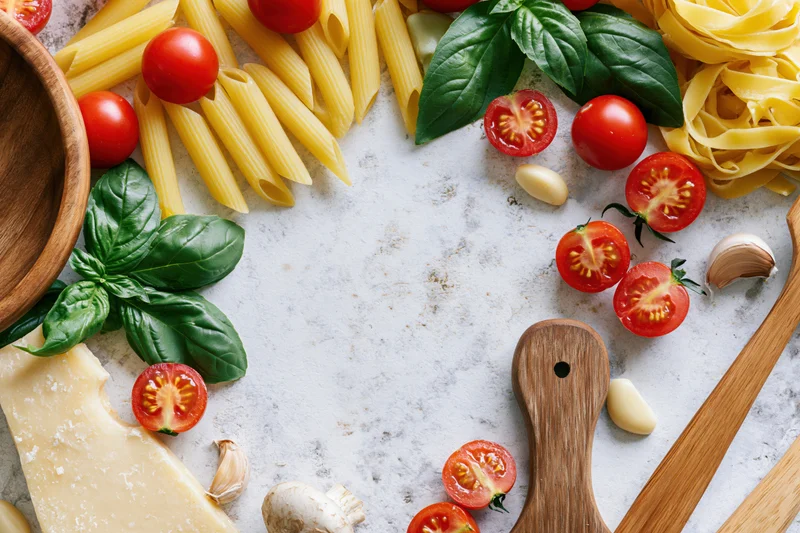 Italian cooking ingredients arranged in a flat lay border on a marble countertop with copyspace in center