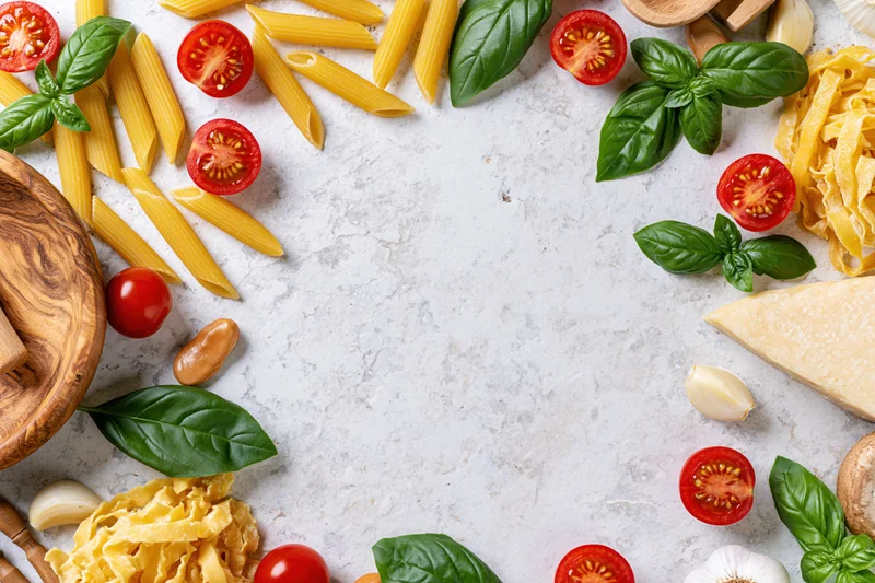 Italian cooking ingredients arranged as a flat lay border on a white marble surface