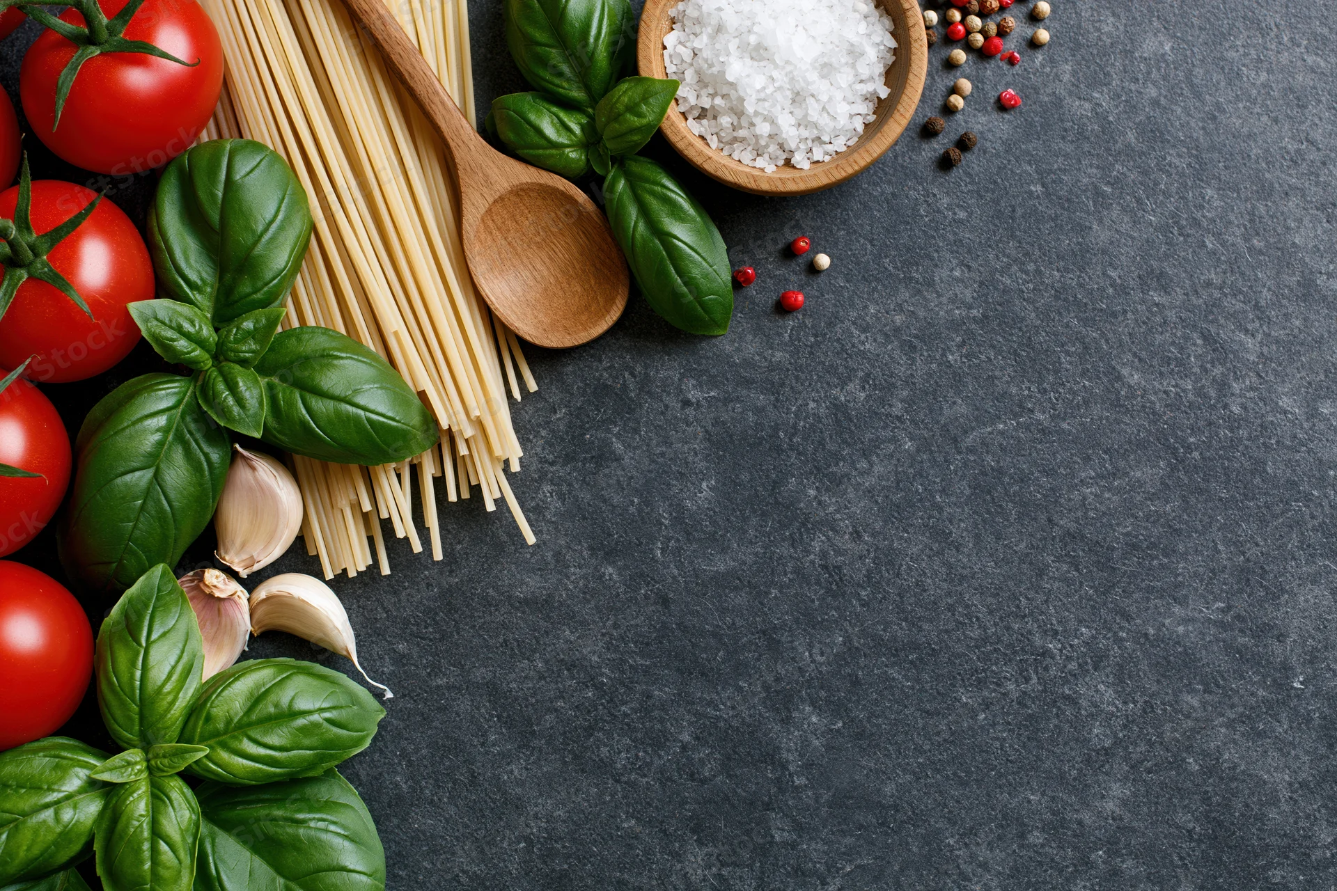 Italian pasta ingredients arranged along left edge of dark stone countertop with copyspace on right