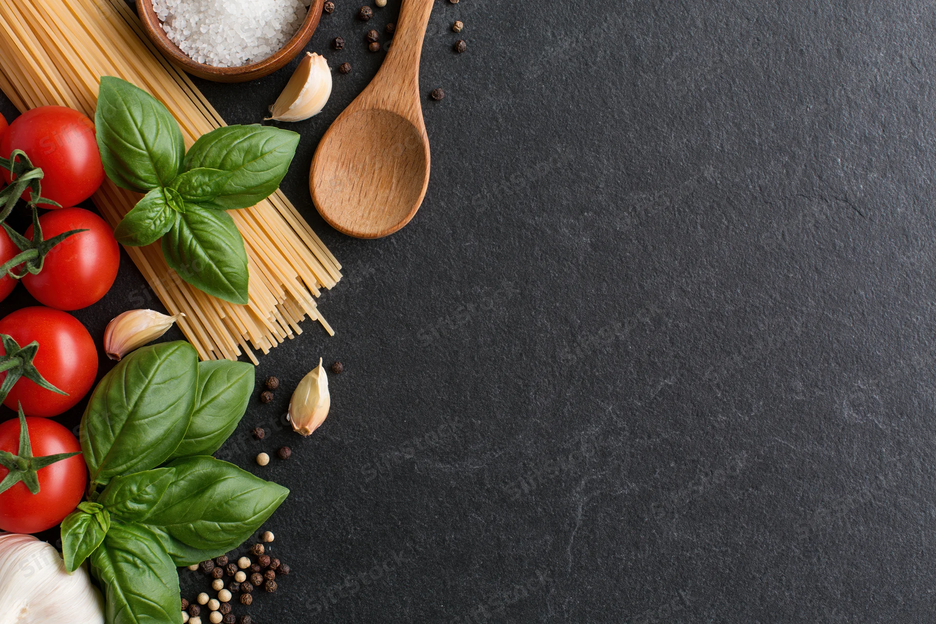 Italian pasta ingredients arranged along left edge of dark slate surface with copyspace
