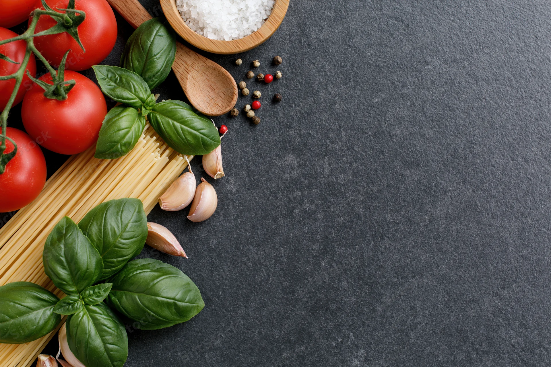 Italian pasta ingredients arranged along the left edge of a dark surface with copyspace on the right