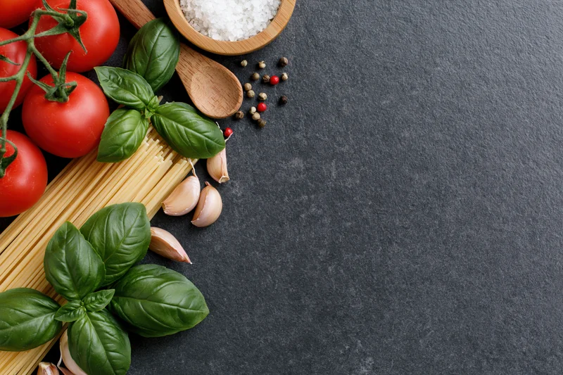 Italian pasta ingredients arranged along the left edge of a dark surface with copyspace on the right